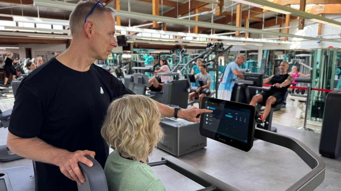 Trainer erklärt einem Mitglied die Werte am Display auf der Trainingsfläche
