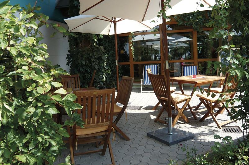 Sonnenterrasse des Bistros mit Holzstühlen unter Sonnenschirmen