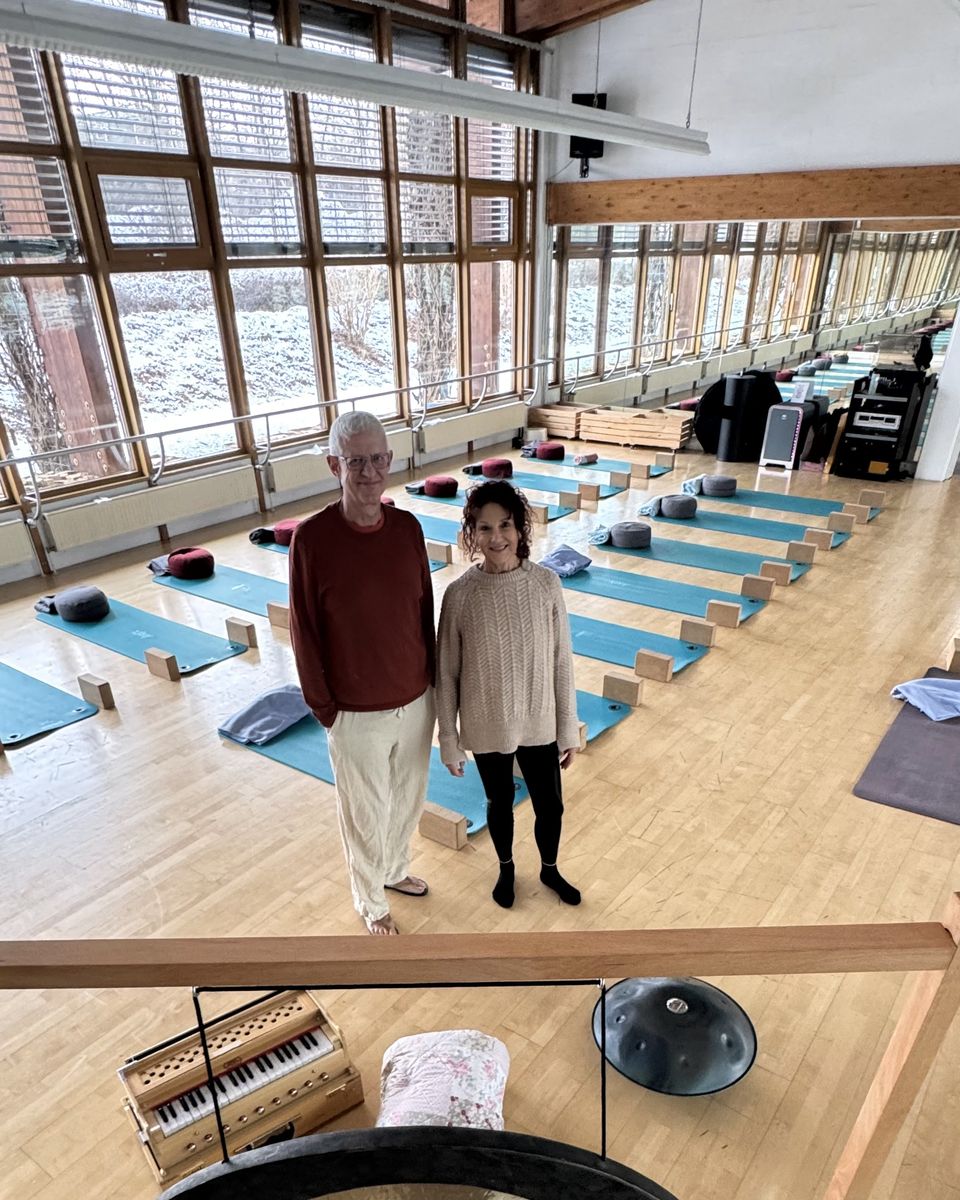 Kursraum mit ausgelegten Yogamatten und Gong, zwei Menschen im Gespräch