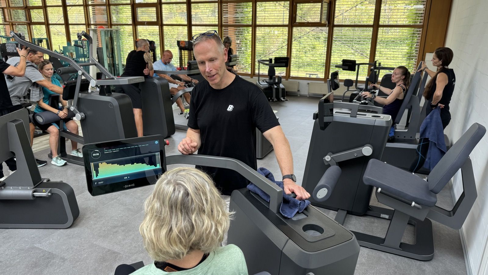 Trainer erklärt einem Mitglied die Werte auf dem Display des Milon-Geräts