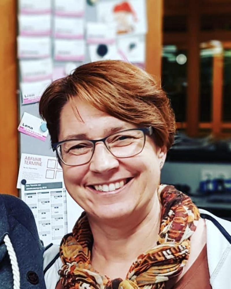 Moni mit Brille und Tuch lächelt in die Kamera
